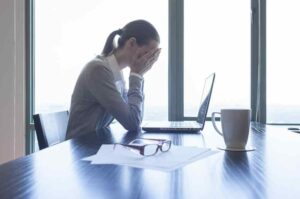 Woman appointed excecutor of a will sitting infront of her computer covering her face with her hands in an overwhelmed fashion